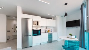 A modern kitchen with white cabinetry, stainless steel appliances, and a dining area with a blue chair.