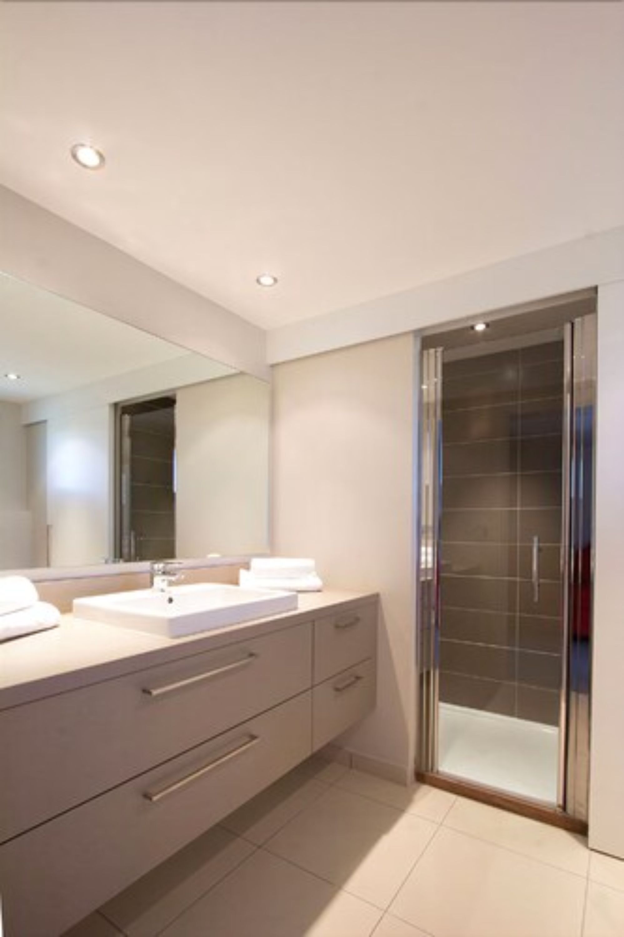 A modern bathroom with a large mirror, two sinks, and a glass shower enclosure.