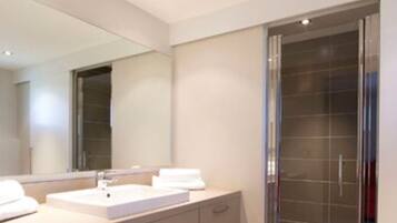 A modern bathroom with a large mirror, two sinks, and a glass shower enclosure.