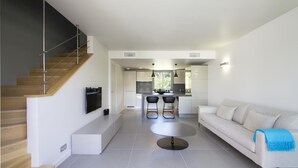 Una sala de estar moderna con una escalera, un sofá, una mesa redonda y una cocina al fondo.