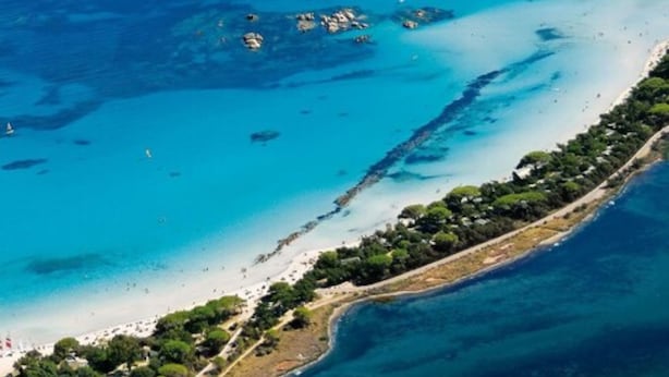 Vista aérea de una zona costera con aguas turquesas cristalinas, afloramientos rocosos y una franja de tierra con vegetación densa.