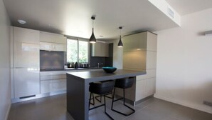 Una cocina moderna con una isla central, taburetes de bar, iluminación colgante y vistas al exterior.