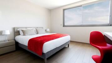 A hotel room with a bed, a desk, and a window.