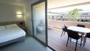 Habitación de hotel moderna con cama, puerta de vidrio que da a una terraza exterior con mesa y sillas, y vista de los edificios circundantes.