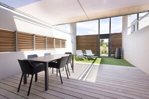 Terrassa exterior moderna amb un deck de fusta, taula de dinar amb cadires i zona de seients amb gandules.