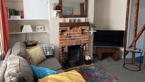 A living room with a brick fireplace, a sofa with cushions, a television, and a bookshelf.