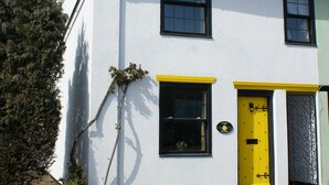 A white building with a yellow door, a chimney, and a small garden area.