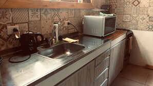 Una cucina con lavello in acciaio inossidabile, macchina da caffè, forno a microonde e una finestra sopra il lavello.