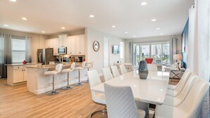 A modern kitchen with white cabinets, a central island with bar stools, and a dining area with a white table and chairs.