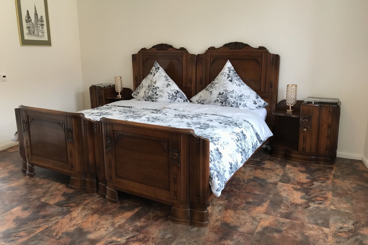 A wooden four-poster bed with a floral bedspread and matching pillows, flanked by nightstands with lamps.