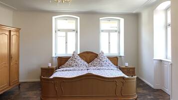 A bedroom with a wooden bed, two windows, a chandelier, and a wardrobe.