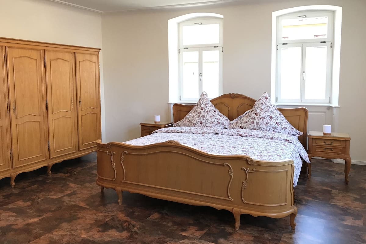A bedroom with a wooden bed, two bedside tables, a wardrobe, and two windows.