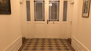 Un couloir avec des carreaux de sol à motifs, des portes à deux battants avec des panneaux de verre et un lustre.
