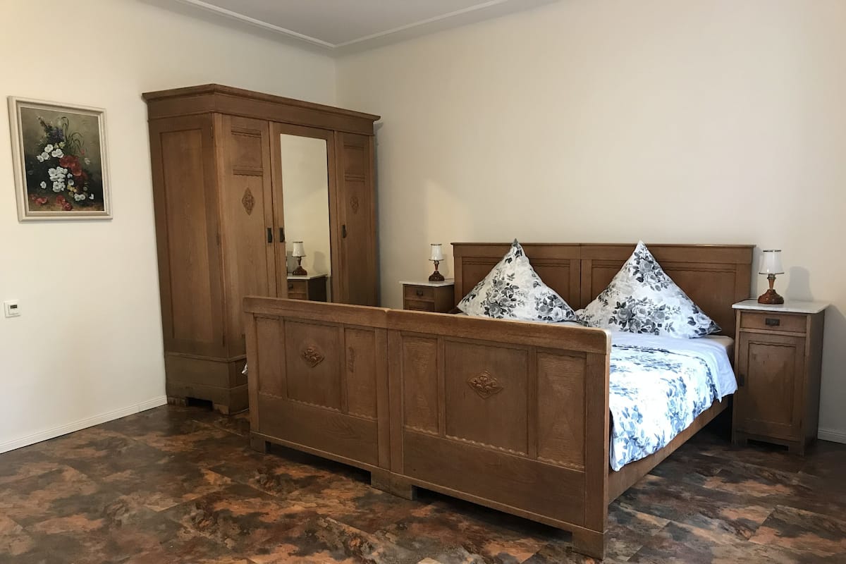 A bedroom with a wooden bed, two nightstands, a wooden wardrobe, and a floral painting on the wall.