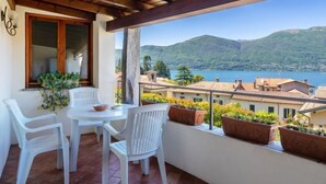 Un balcone con tetto in legno, sedie in plastica bianca, un tavolino rotondo e vasi in terracotta.