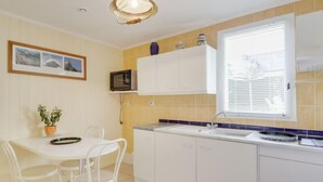 A compact kitchen with white cabinets, a microwave, a sink, and a window with blinds. - Les Genêts by Interhome (La Richardais)