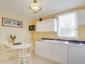 A compact kitchen with white cabinets, a microwave, a sink, and a window with blinds.