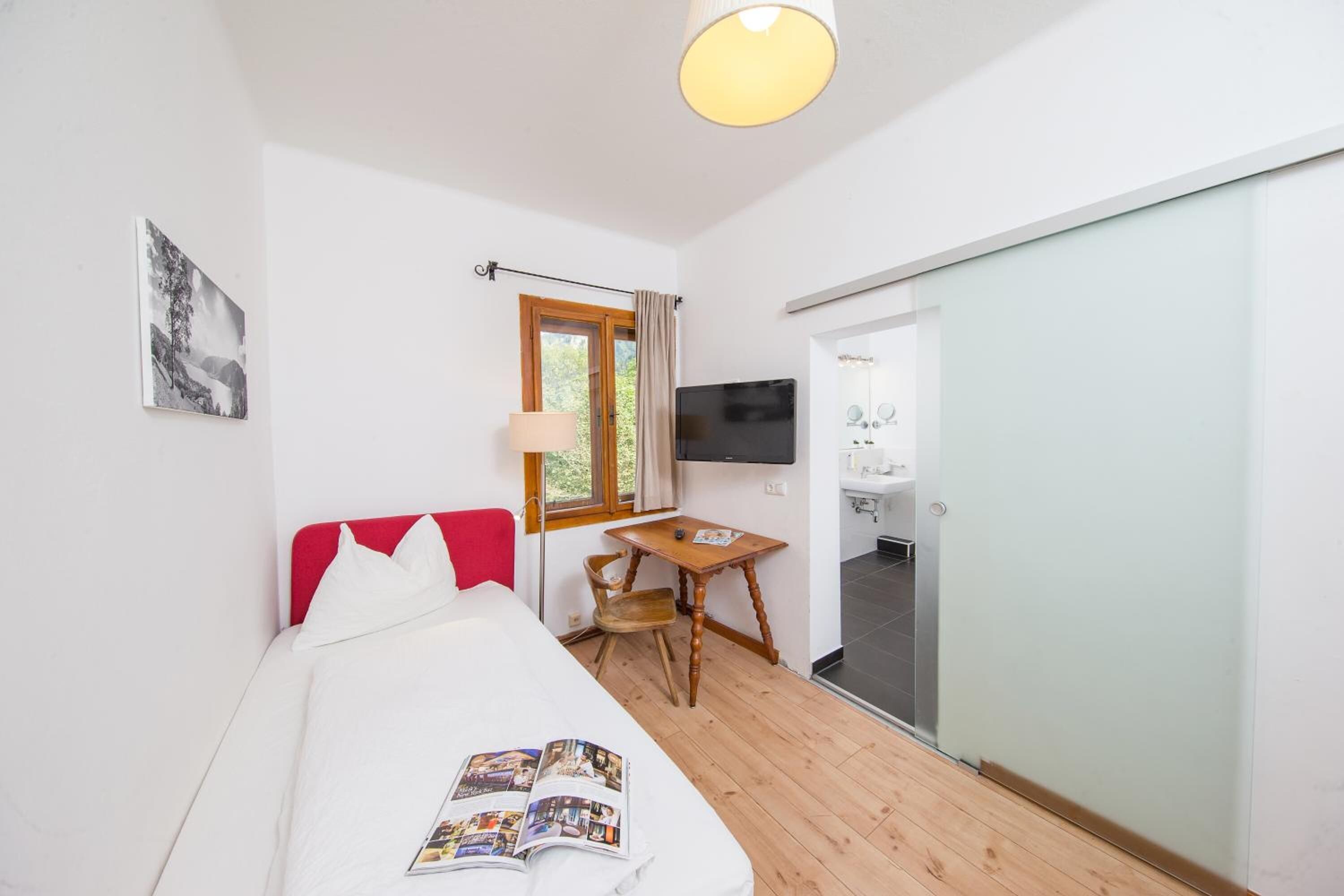 Une chambre à coucher comprenant un lit, un bureau, une chaise, un téléviseur et une porte coulissante donnant sur une salle de bain.