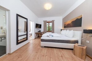 Un dormitorio moderno con una cama grande, televisor, escritorio y ventana con cortinas.