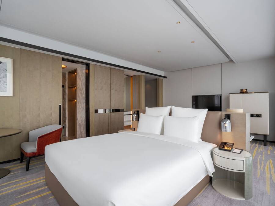 Habitación de hotel con una cama grande, un escritorio, una silla, un armario y una mesita de noche con lámpara.