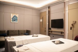 A hotel room with two beds, a sofa, a television, and a painting on the wall.