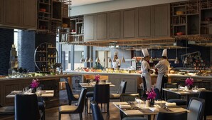 A modern restaurant with a central bar area, multiple dining tables, and a kitchen in the background. - Pullman Suzhou Zhonghui (Suzhou)