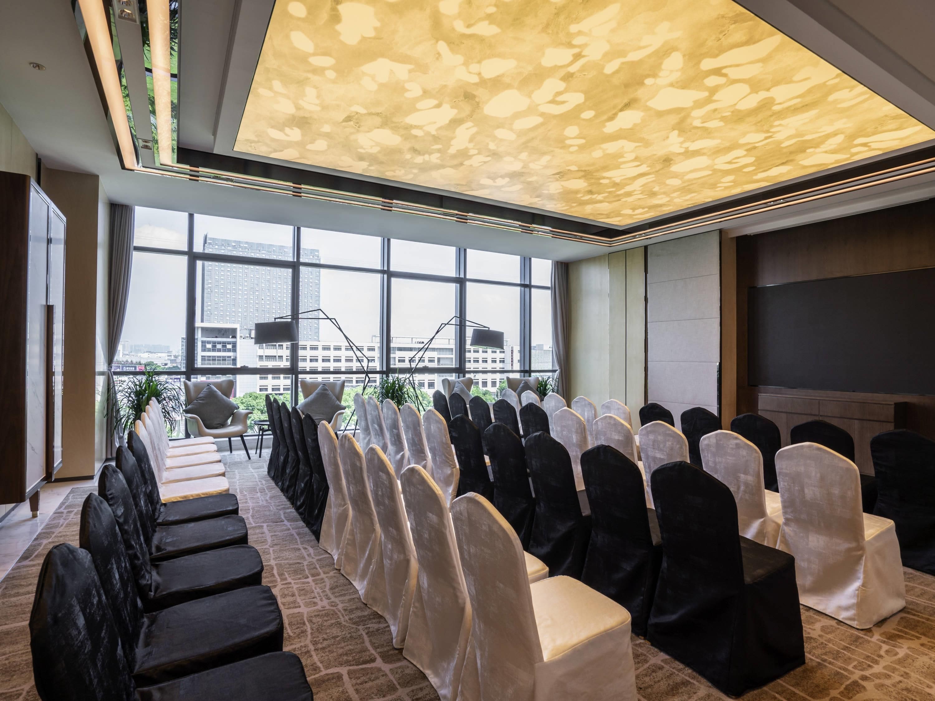 A conference room with rows of chairs, a large window with a city view, and a modern ceiling design.
