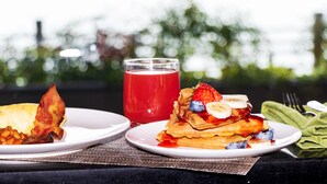 Two plates of food, one with waffles topped with fruit and the other with bacon and beans, and a glass of red drink on a table with a view of trees. - Pullman Suzhou Zhonghui (Suzhou)