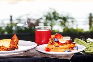 Two plates of food, one with waffles topped with fruit and the other with bacon and beans, and a glass of red drink on a table with a view of trees. - Pullman Suzhou Zhonghui (Suzhou)