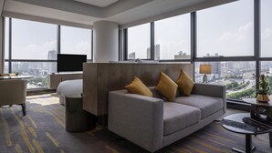 A modern hotel room with a sofa, armchair, and a TV. Large windows offer a city view. - Pullman Suzhou Zhonghui (Suzhou)