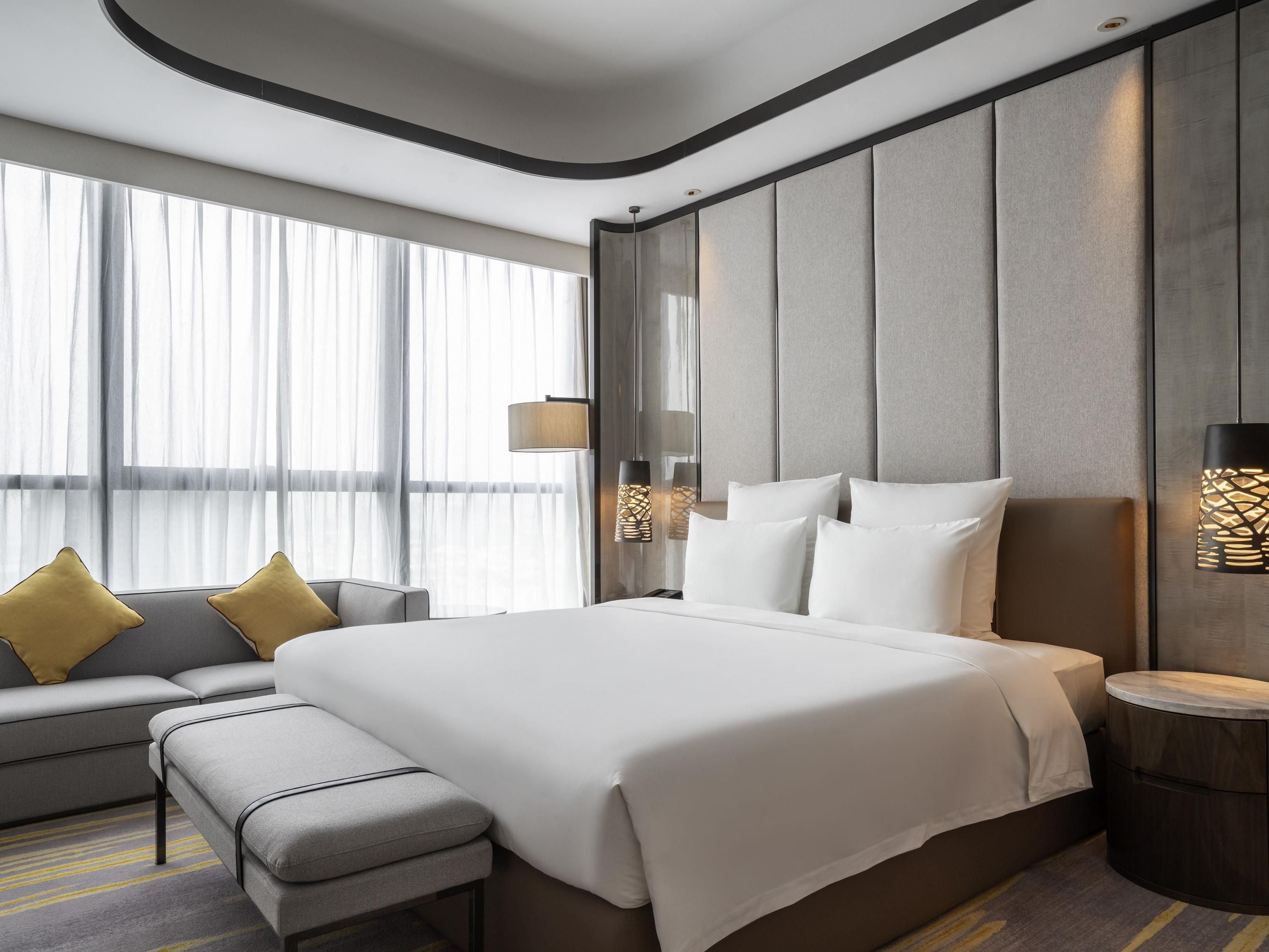 A modern hotel room with a large bed, a sofa, and a bench.