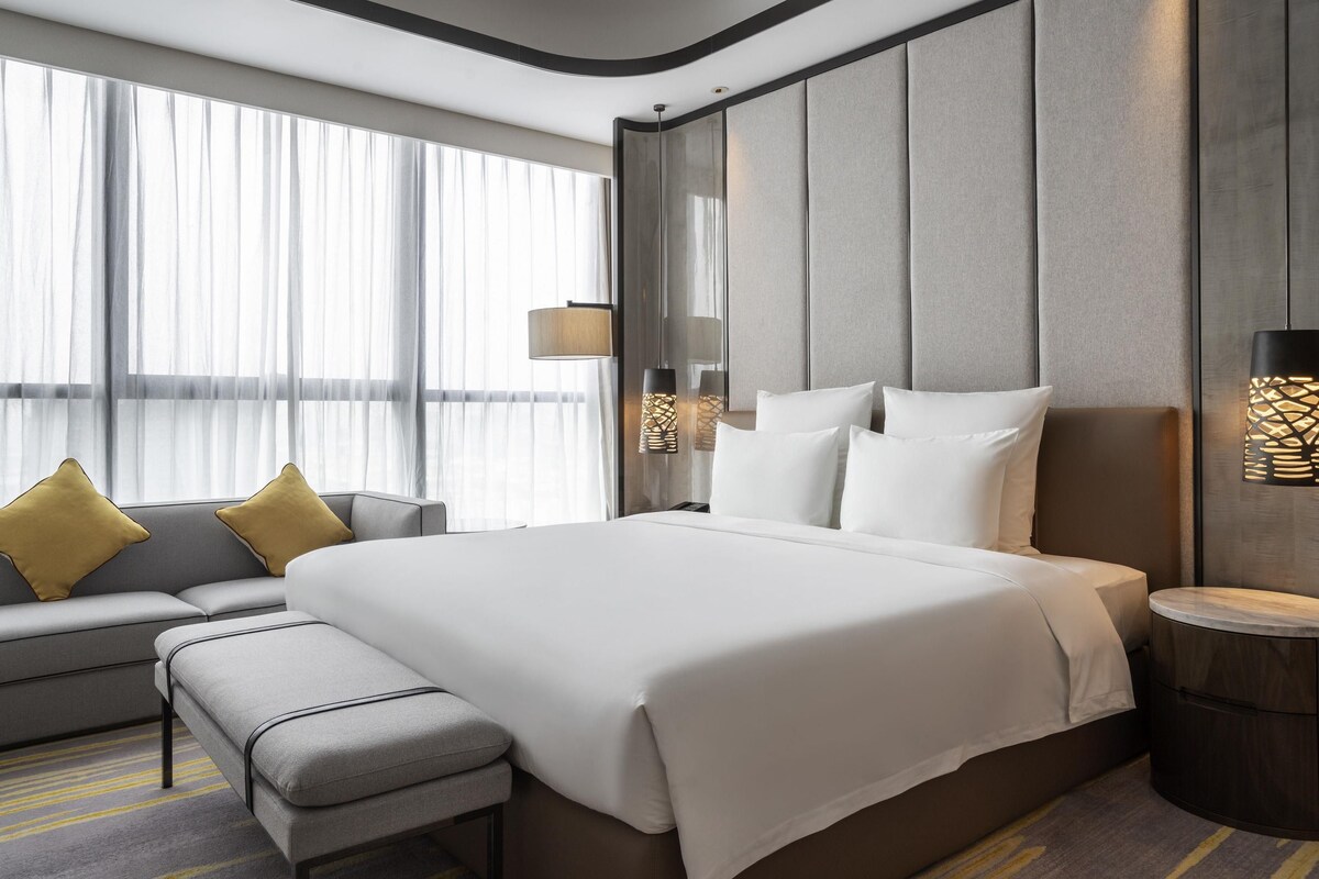 A modern hotel room with a large bed, a sofa, and a bench.