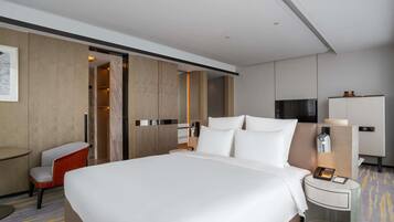 A modern hotel room with a large bed, a bedside table with a lamp, a chair, and a wardrobe.