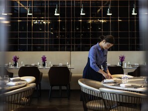 A restaurant with tables set for dining, a waiter attending to a table, and a modern interior design with pendant lighting. - Pullman Suzhou Zhonghui (Suzhou)