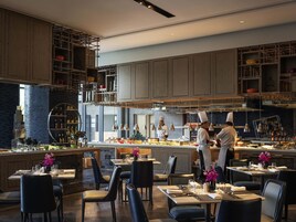 Un restaurante moderno con una barra central, varias mesas para comer y una cocina al fondo.