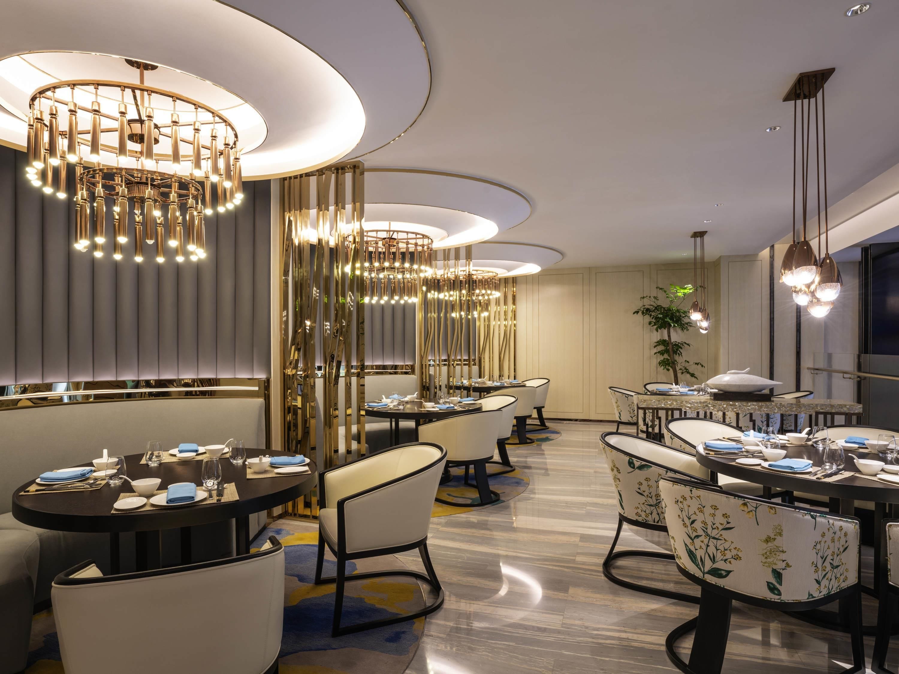 A modern dining area with round tables, chairs, and multiple chandeliers.