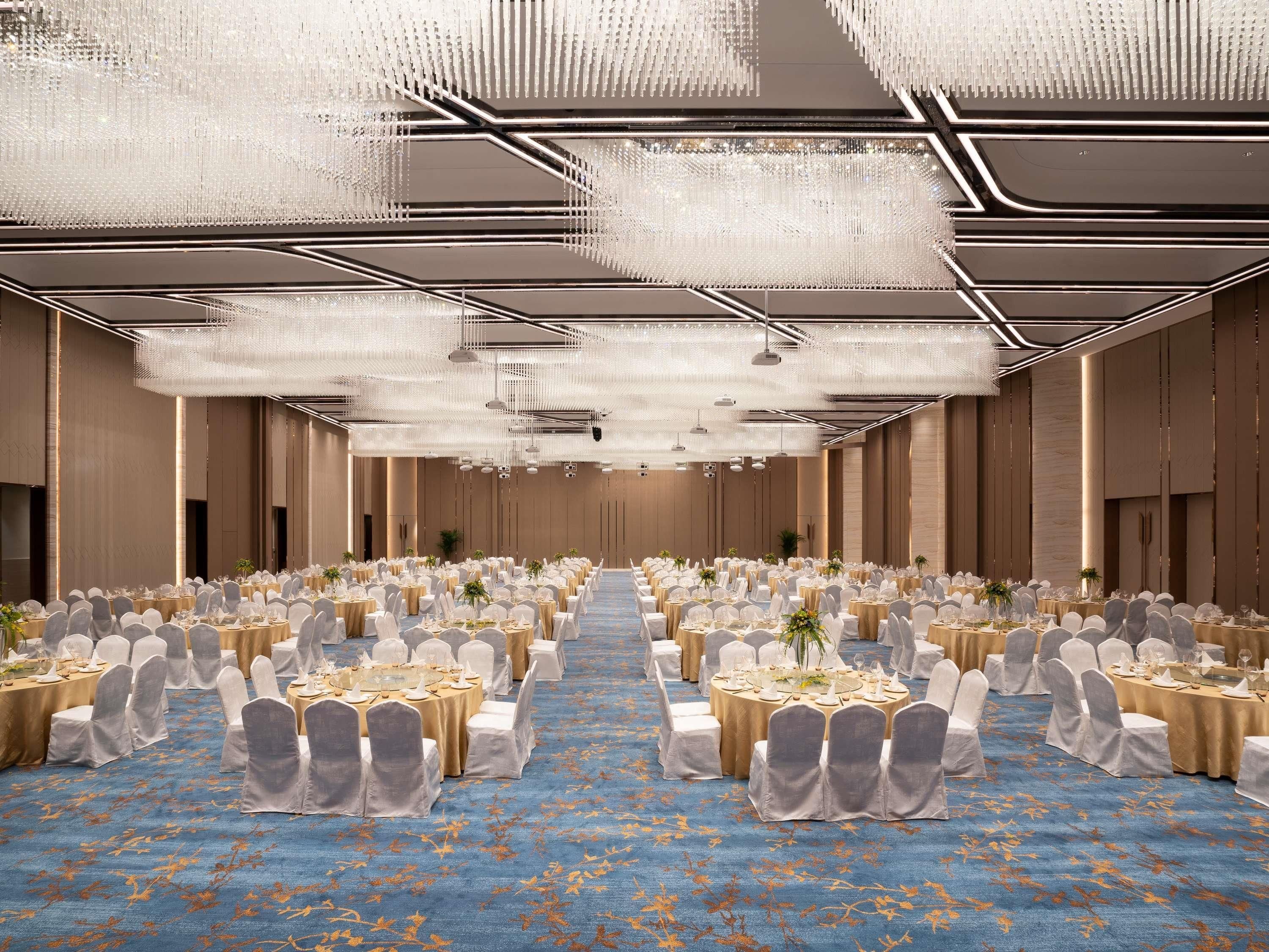 A banquet hall with round tables, white chairs, and a blue carpet.