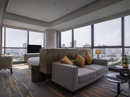 Habitación de hotel moderna con sofá, sillón y televisión. Amplias ventanas con vistas a la ciudad.