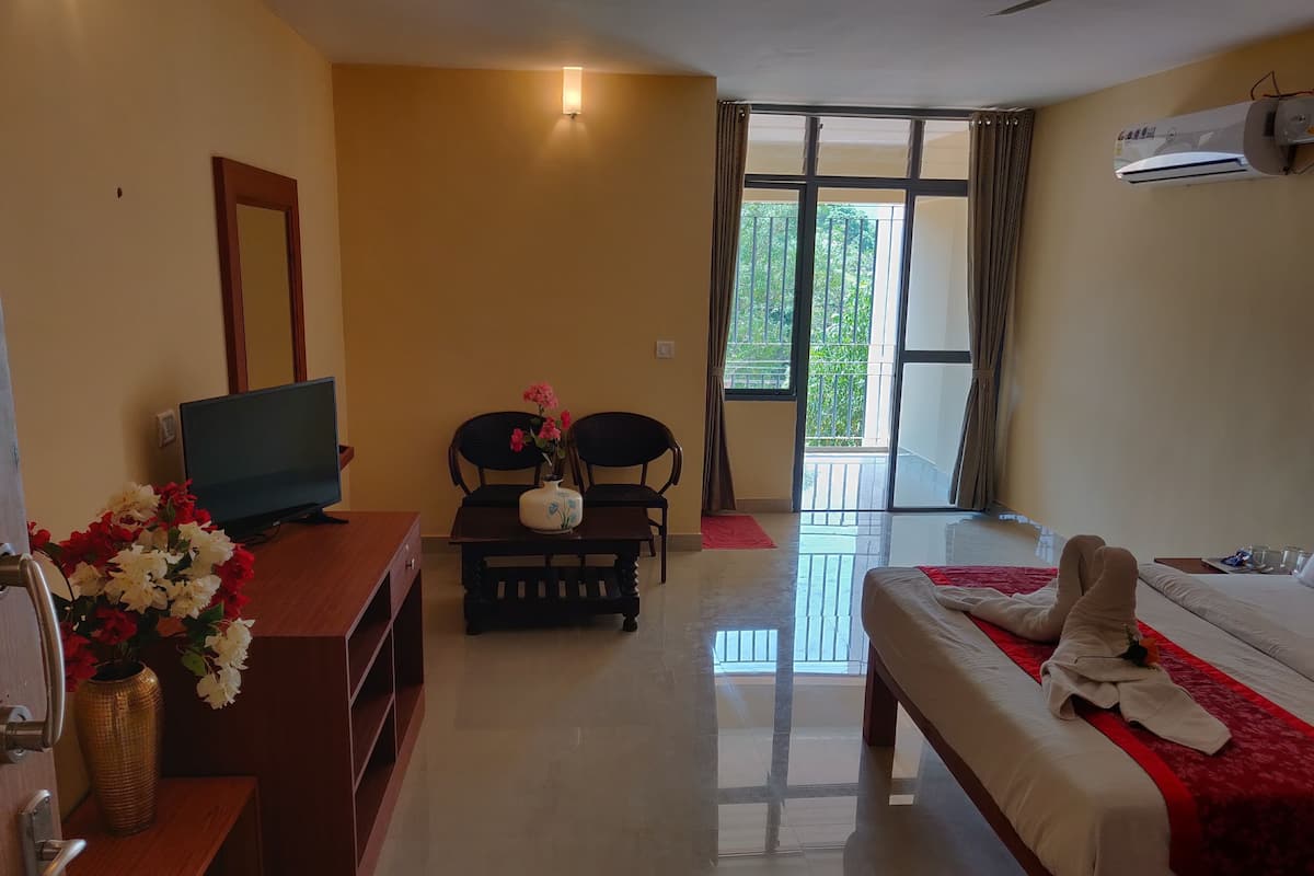 Habitación de hotel con cama, televisión, escritorio con un florero, sillas y un balcón con vistas.
