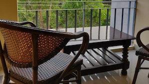 A balcony with a view of lush greenery and trees. There are two wicker chairs and a small table. - Paradise Wild Hills (Hosanagara)