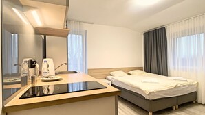 Una moderna camera d'hotel con angolo cottura, un letto e un'ampia finestra con tende.
