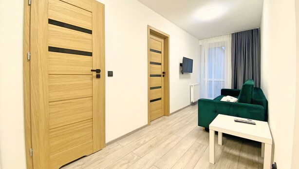 Una stanza moderna con porte in legno, un divano verde, un tavolo bianco e una TV appesa al muro.