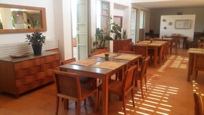 Una zona de dinar amb diverses taules i caires de fusta, un mostrador tipus bufet amb una planta en test i un gran mirall a la paret.
