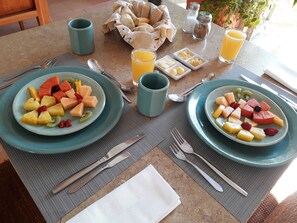 A breakfast table with two plates of fruit, two glasses of orange juice, and a small bowl of butter. - Hotel Alto del Viento (Barichara)