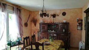 Een eethoek met een tafel gedekt voor vier personen, omringd door stoelen. Daarboven hangt een kroonluchter, en aan de rechterkant een kast met decoratieve objecten.