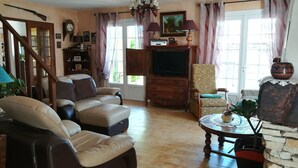 Een woonkamer met een bank, fauteuil, televisie, houten kast en een stenen muur.