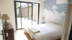 A bedroom with a bed, a desk, a chair, a lamp, and a sliding glass door leading to an outdoor area. - Villa bottom T3 300 meters from the beach (Arcachon)
