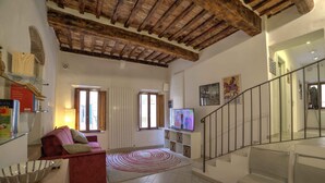 Ein geräumiger Wohnbereich mit hoher Holzbalkendecke, einem roten Sofa, einem Glastisch und einer Treppe mit Glastrennwand.