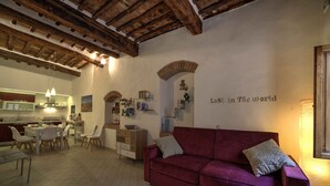 Ein gemütliches Wohnzimmer mit einem roten Sofa, einem Essbereich mit Stühlen, einer Küche im Hintergrund und einer Wand mit einer dekorativen Nische und dem Text 