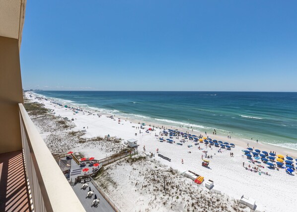 Ein Strand mit weißem Sand, blauen Sonnenschirmen und einem klaren Himmel.